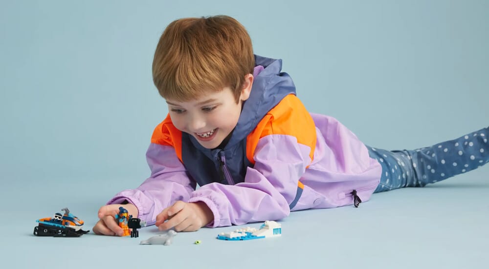 Dziecko leżące i bawiące się skuterem śnieżnym LEGO City Arctic i figurkami odkrywców