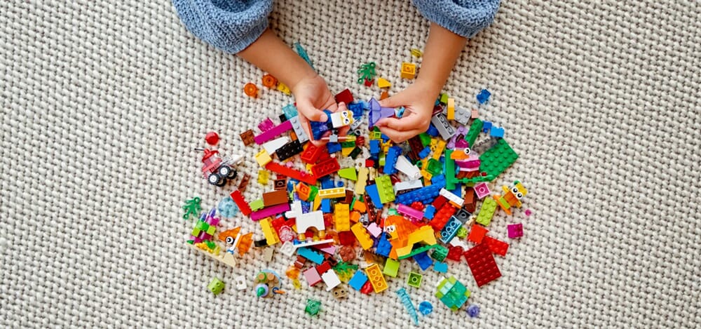 Dziecięce ręce sortujące kolorowe klocki LEGO Classic na kremowym dywanie