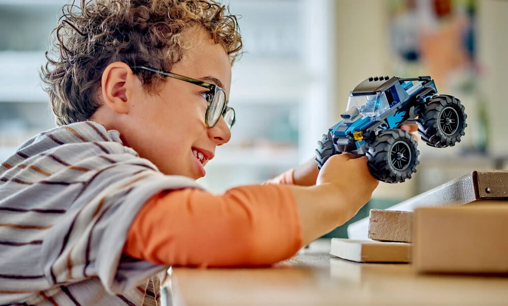 Dziecko bawiące się niebieskim monster truckiem LEGO z dużymi kołami