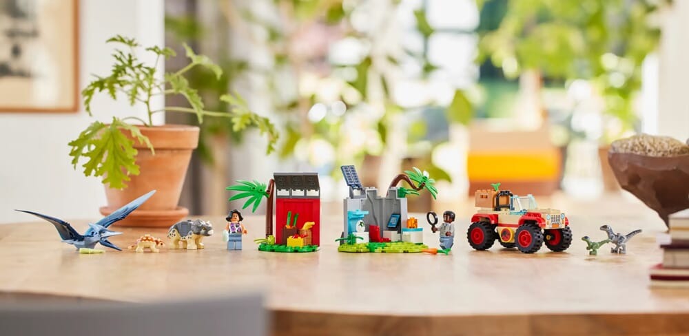 Ekspozycja zestawów LEGO Jurassic World z dinozaurami i pojazdami oraz minifigurkami na drewnianym stole