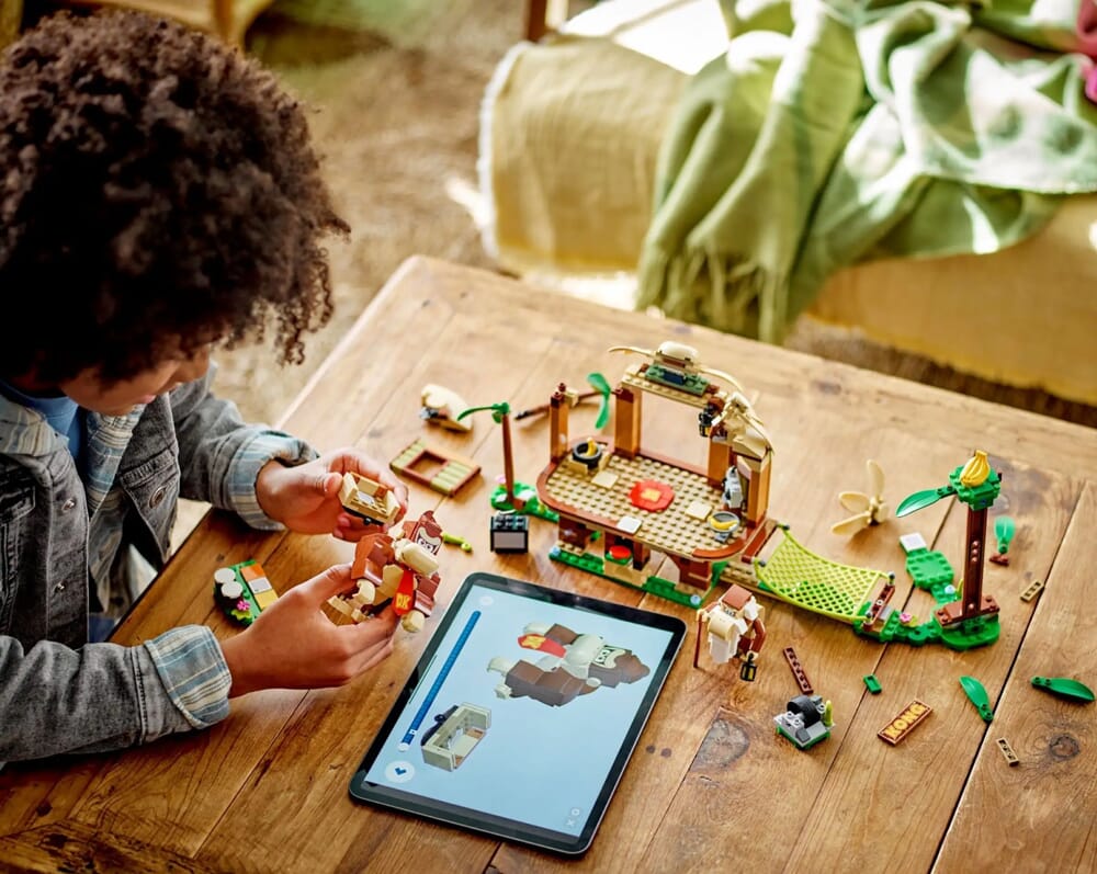 Dziewczynka w dżinsowej kurtce korzystająca z cyfrowych instrukcji budowania LEGO na tablecie podczas składania Domku na drzewie Donkey Konga