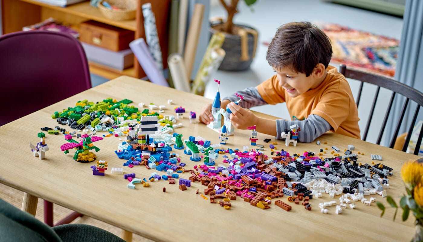 Chłopiec w pomarańczowej koszuli sortujący kolorowe klocki LEGO według koloru na drewnianym stole