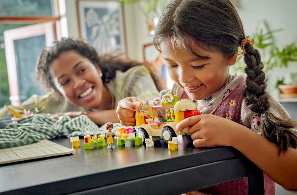 Mädchen spielt mit LEGO Friends Food Truck Set zusammen mit Elternteil