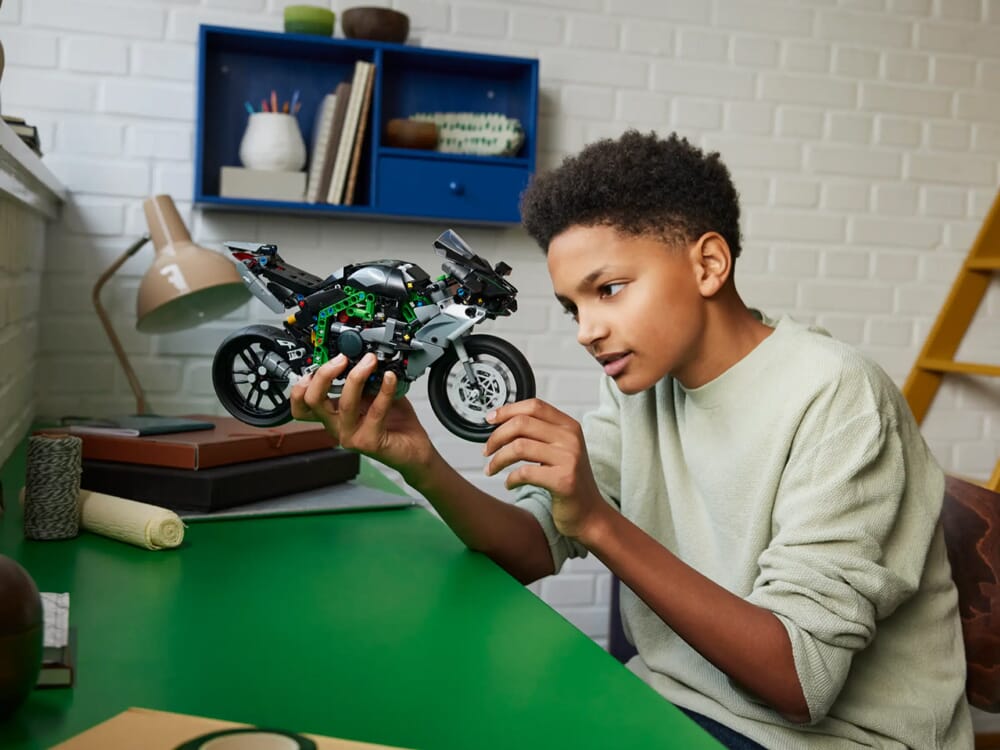 Bambino con maglione color crema che esamina la moto LEGO Technic Kawasaki su scrivania verde