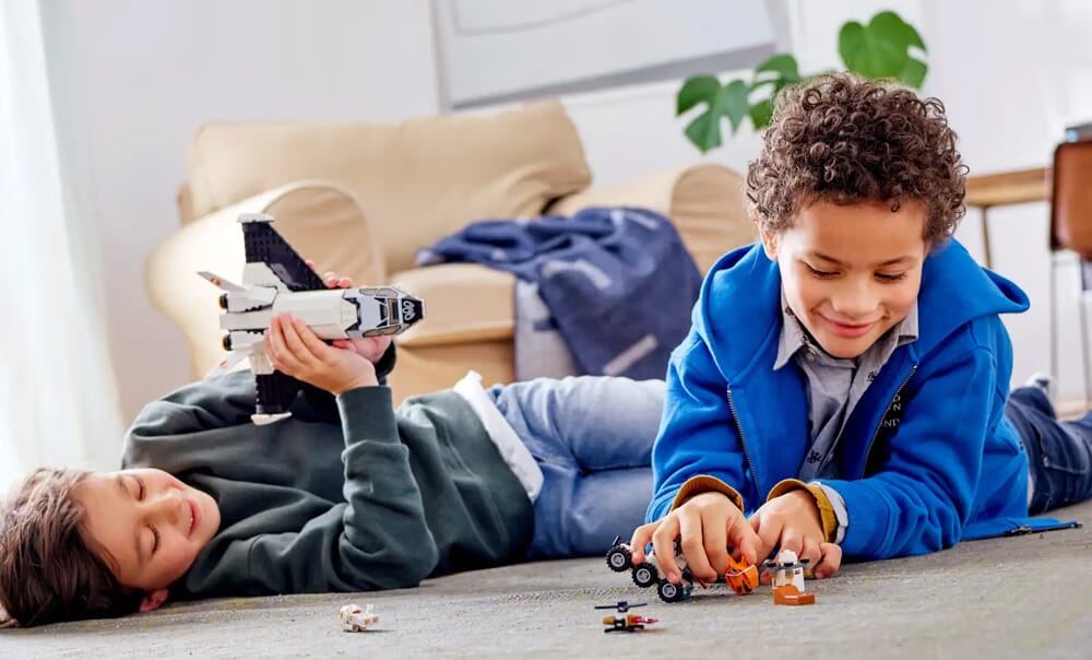 Dwoje dzieci leżących na podłodze i bawiących się zestawami LEGO z promem kosmicznym i pojazdami