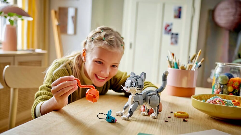 Dziewczynka w zielonym swetrze bawiąca się zestawem figurki kota LEGO Creator 3-w-1